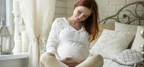 beyaz giyinmiş yatakta oturan hamile kadın