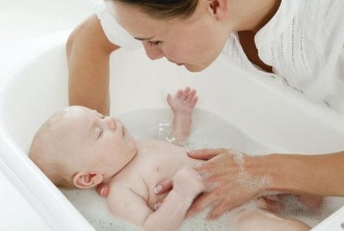 bebek küvetinde bebeğine banyo yaptıran anne