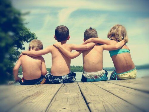 sırtı dönük deniz kenarında kol kola oturan dört çocuk
