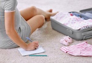 Bebek bavulunun önünde oturup not alan anne