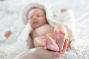 Annesinin ayaklarını tuttuğu yatakta yatan bebek