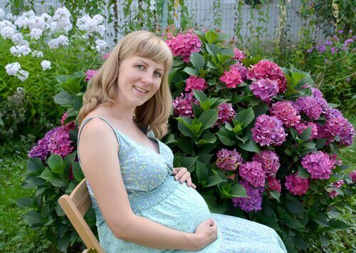 Çiçeklerin önünde mavi elbisesiyle oturan hamile kadın