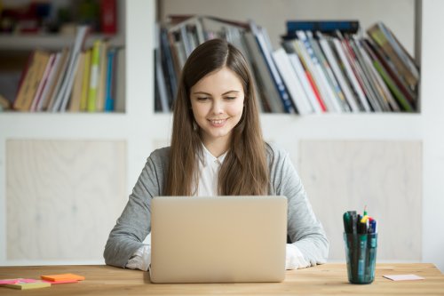 Masada oturmuş bilgisayara bakarak gülümseyen kız