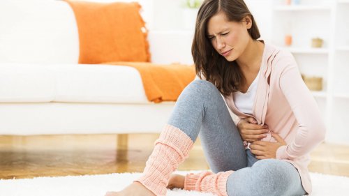 Ağrıdan ötürü yerde oturmuş karnını tutan kadın