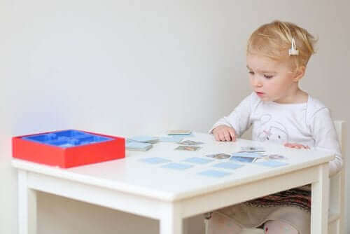 küçük çocuk bir masada oturmuş kartlarla hafıza oyunu oynuyor