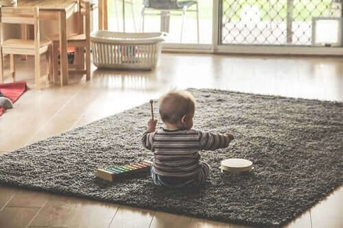 küçük bebek halının üstünde oturmuş müzik aletleriyle oynuyor