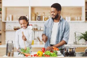 Mutfakta baba biber kesiyor kızı salatayı karıştırıyor.