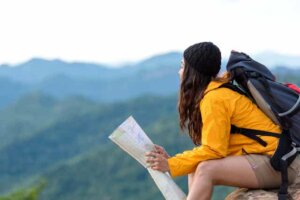 Bir kadın doğada bir taşa oturmuş elinde harita var.
