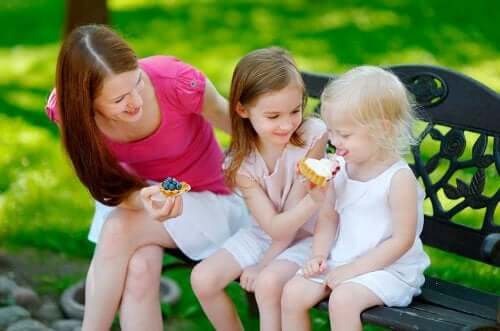 Çocukları ile bir parkta tatlı yiyen bir anne.